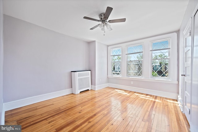 unfurnished room with baseboards, light wood-style flooring, radiator, and ceiling fan