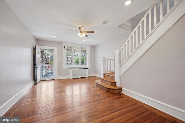 entrance foyer featuring wood finished floors, baseboards, radiator heating unit, stairway, and a ceiling fan