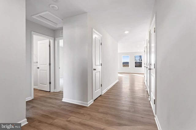 hall featuring baseboards, attic access, and wood finished floors