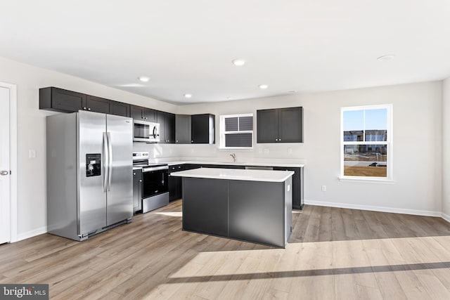 kitchen featuring a center island, light wood-type flooring, light countertops, dark cabinets, and stainless steel appliances