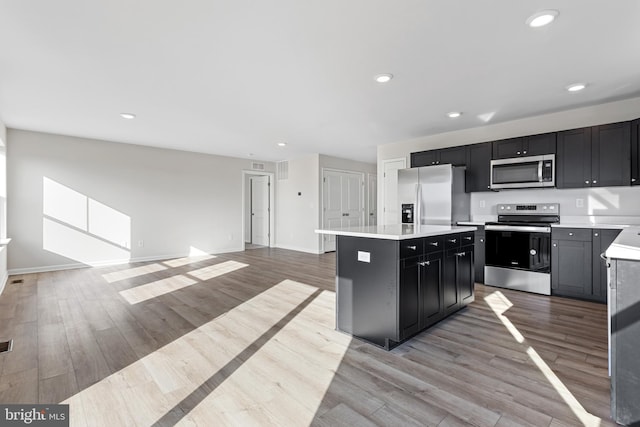 kitchen featuring a center island, light countertops, dark cabinets, light wood finished floors, and appliances with stainless steel finishes