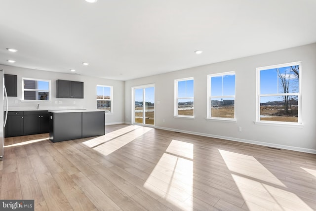 unfurnished living room featuring baseboards, recessed lighting, light wood finished floors, and a sink