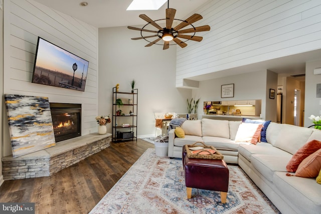 living area featuring wooden walls, a ceiling fan, a large fireplace, and wood finished floors