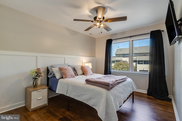 bedroom featuring dark wood-type flooring, baseboards, ceiling fan, and a wainscoted wall