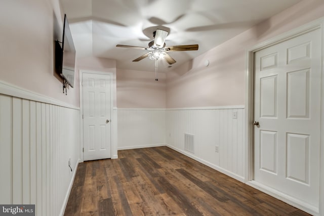 empty room featuring visible vents, a ceiling fan, wainscoting, and dark wood-style flooring