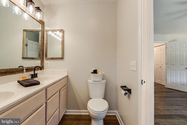 bathroom with a sink, double vanity, toilet, baseboards, and wood finished floors