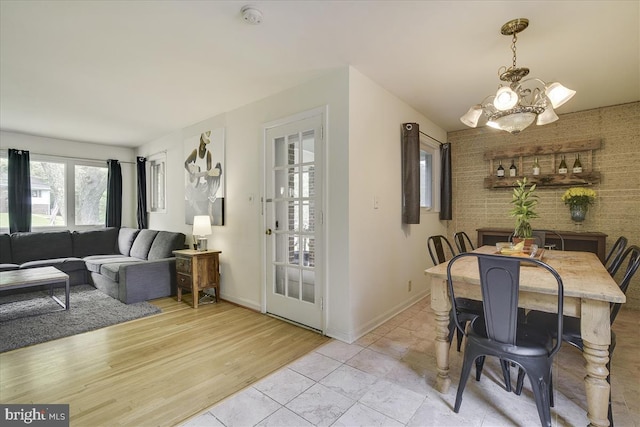 dining area with an inviting chandelier, baseboards, and brick wall