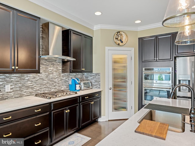 kitchen with crown molding, decorative backsplash, wood finished floors, wall chimney range hood, and appliances with stainless steel finishes