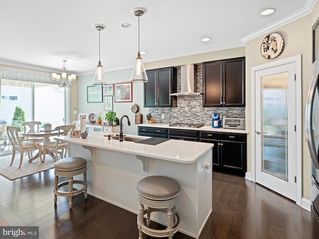 kitchen featuring stainless steel gas stovetop, ornamental molding, a breakfast bar, wall chimney exhaust hood, and dark wood-type flooring