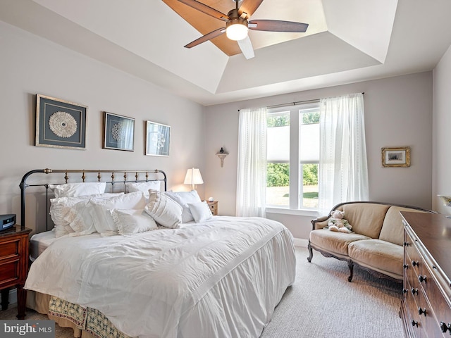 carpeted bedroom with a raised ceiling and a ceiling fan