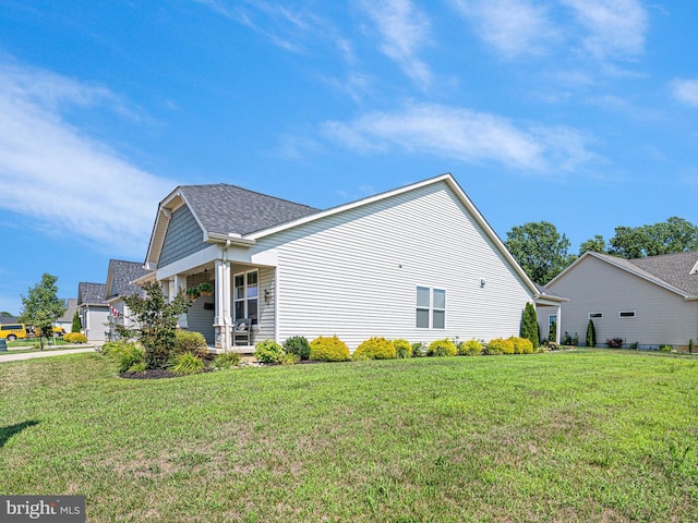 view of side of home with a lawn, covered porch, and roof with shingles