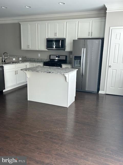 kitchen featuring a sink, light stone counters, crown molding, a center island, and appliances with stainless steel finishes