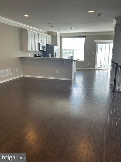 unfurnished living room with dark wood-type flooring, baseboards, and visible vents