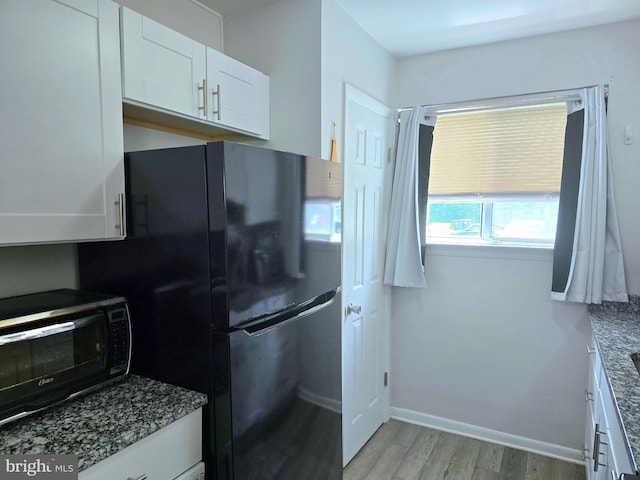 16 Egret Ct, Newark, DE 19702 - kitchen with light wood-style floors, white cabinetry, freestanding refrigerator, dark stone countertops, and baseboards