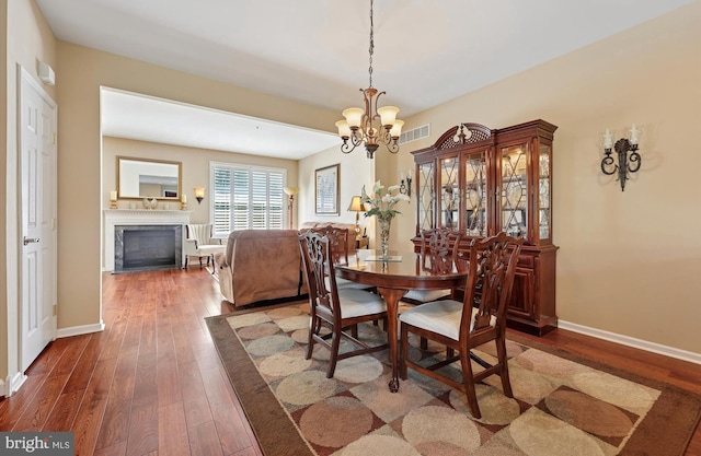 dining room featuring wood-type flooring, visible vents, an inviting chandelier, a glass covered fireplace, and baseboards