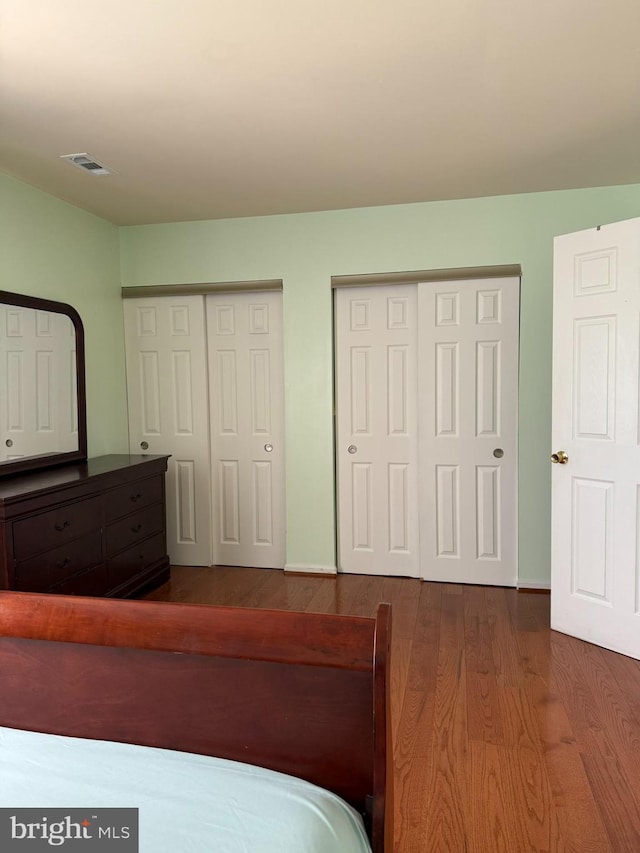 bedroom with visible vents, baseboards, multiple closets, and wood finished floors