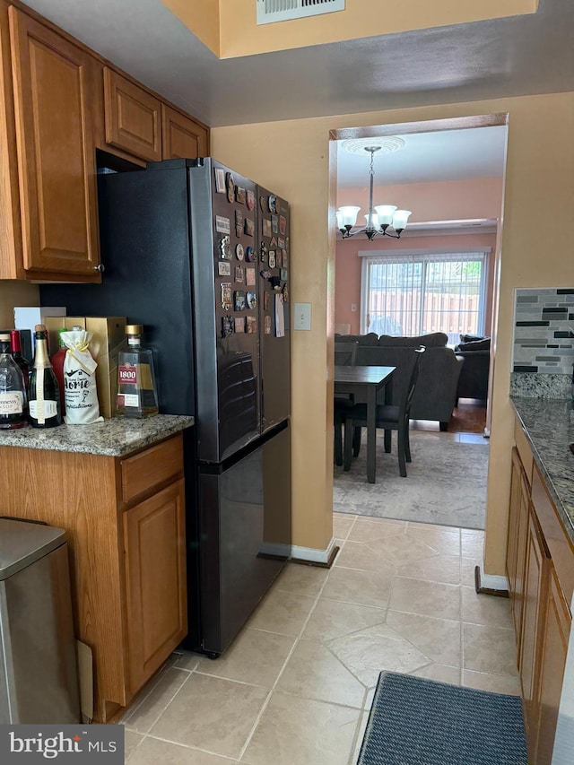 kitchen with dark stone counters, light tile patterned flooring, a notable chandelier, and brown cabinetry