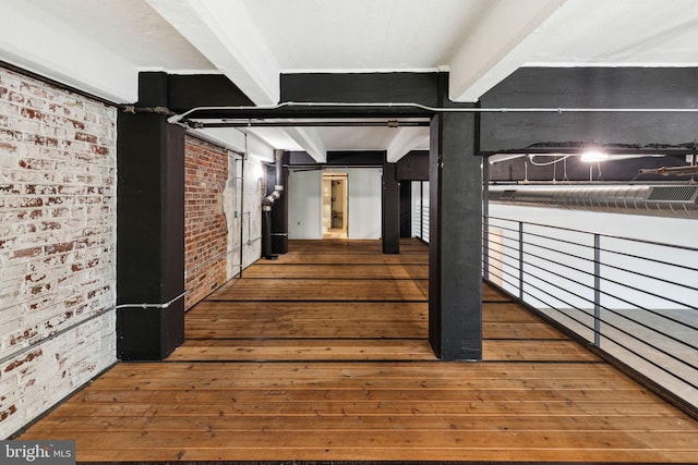 interior space with brick wall, beamed ceiling, and hardwood / wood-style floors