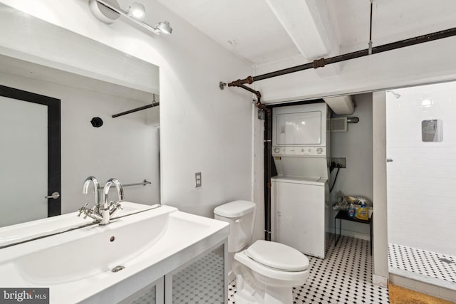 bathroom with toilet, tiled shower, stacked washing maching and dryer, and a sink
