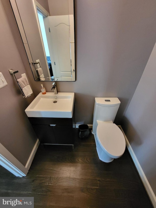 half bath featuring baseboards, wood finished floors, toilet, and vanity