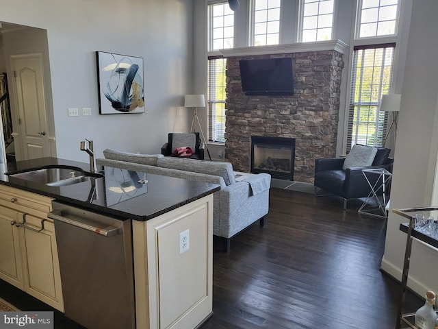 kitchen with dark wood-style flooring, dark countertops, a sink, cream cabinetry, and stainless steel dishwasher