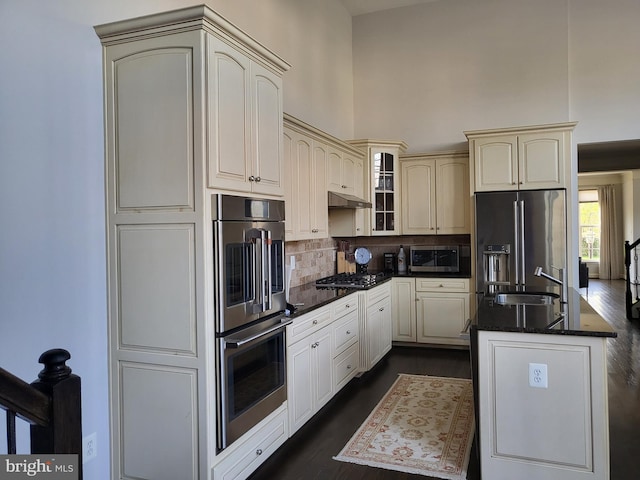 kitchen with dark wood-style flooring, a sink, stainless steel appliances, cream cabinetry, and under cabinet range hood