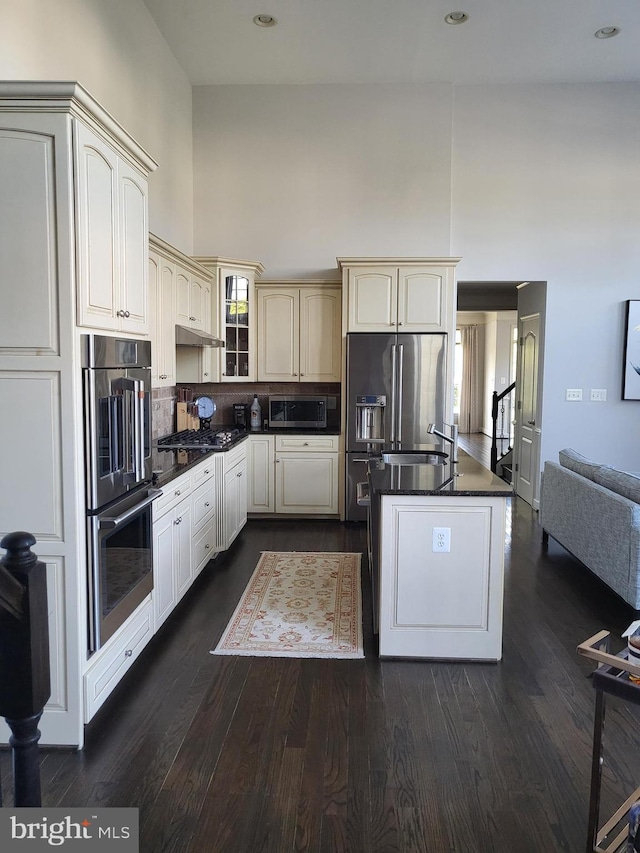 kitchen featuring dark wood-style flooring, dark countertops, a high ceiling, cream cabinetry, and appliances with stainless steel finishes