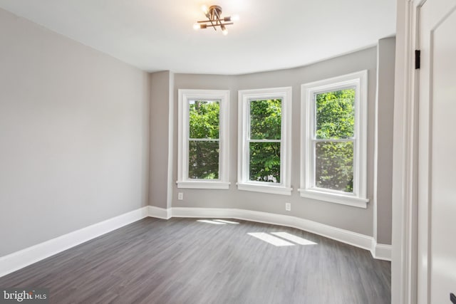 spare room with baseboards, dark wood-style floors, and a notable chandelier