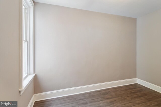 spare room featuring baseboards and dark wood-style floors