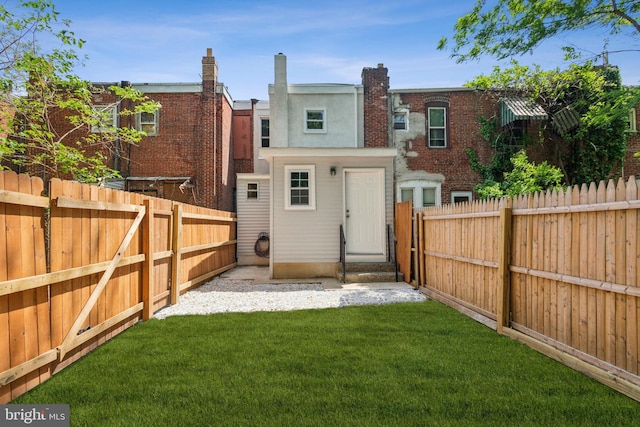 rear view of property featuring entry steps, a lawn, and a fenced backyard