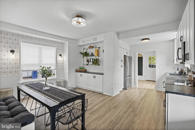 dining room featuring wallpapered walls, a wainscoted wall, and light wood finished floors