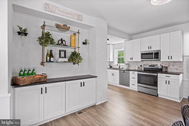kitchen featuring appliances with stainless steel finishes, a sink, dark countertops, and white cabinetry