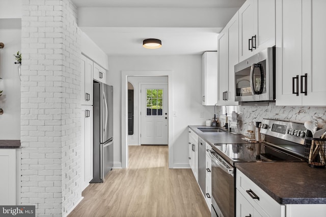 kitchen featuring stainless steel appliances, a sink, light wood-type flooring, dark countertops, and white cabinetry