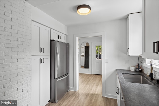 kitchen with freestanding refrigerator, a sink, light wood-style floors, white cabinets, and baseboards