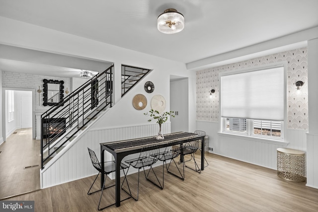 dining room featuring wallpapered walls, wainscoting, wood finished floors, and stairs