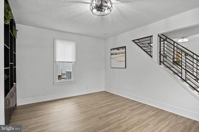 unfurnished room with wood finished floors, baseboards, and stairs