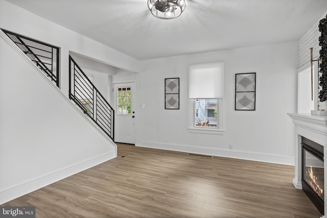 unfurnished living room featuring a large fireplace, stairs, wood finished floors, and baseboards