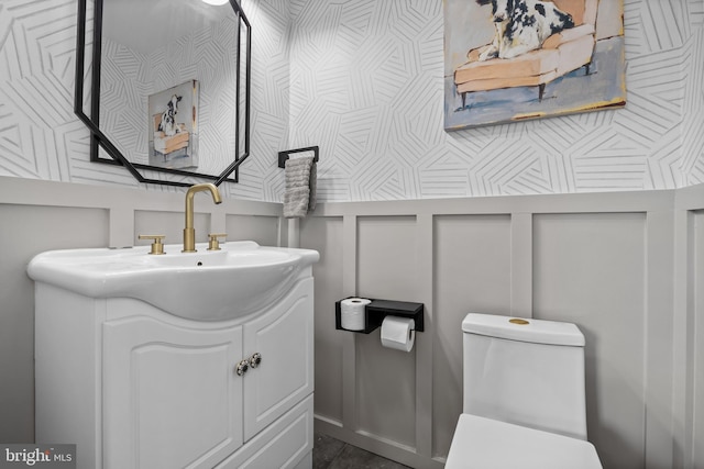 bathroom featuring a decorative wall, toilet, and vanity
