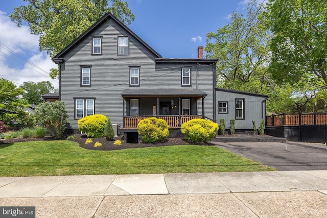 rear view of property with covered porch, a chimney, and a lawn