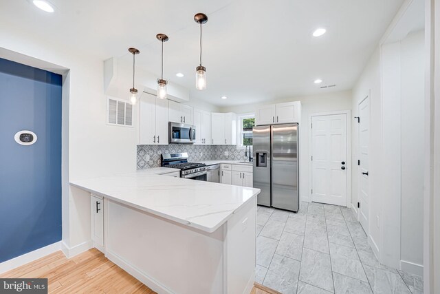 1621 Lyman Pl NE, Washington, DC 20002 - kitchen with appliances with stainless steel finishes, a peninsula, light stone counters, tasteful backsplash, and white cabinetry
