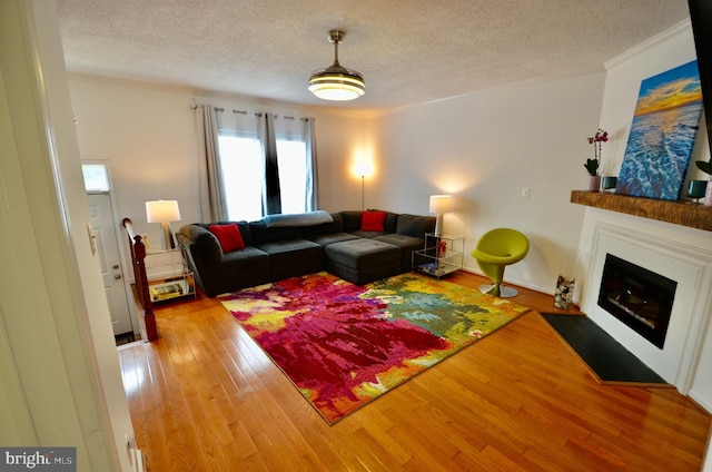 living room with crown molding, a fireplace with flush hearth, a textured ceiling, and wood finished floors