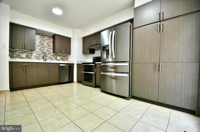 kitchen with light countertops, under cabinet range hood, tasteful backsplash, a sink, and stainless steel appliances