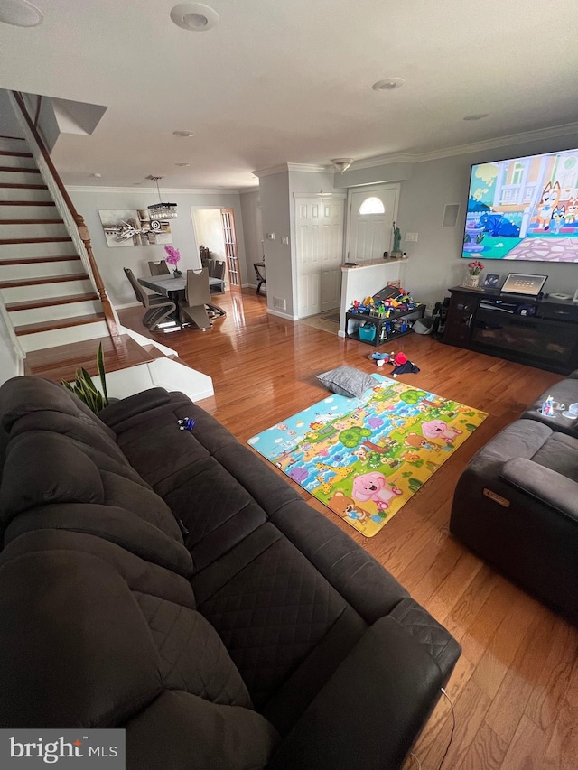 living room featuring crown molding, light wood-type flooring, and stairs