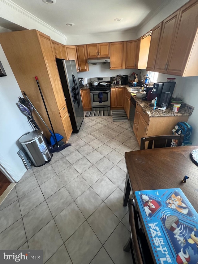 kitchen featuring light tile patterned flooring, appliances with stainless steel finishes, brown cabinetry, dark stone counters, and under cabinet range hood
