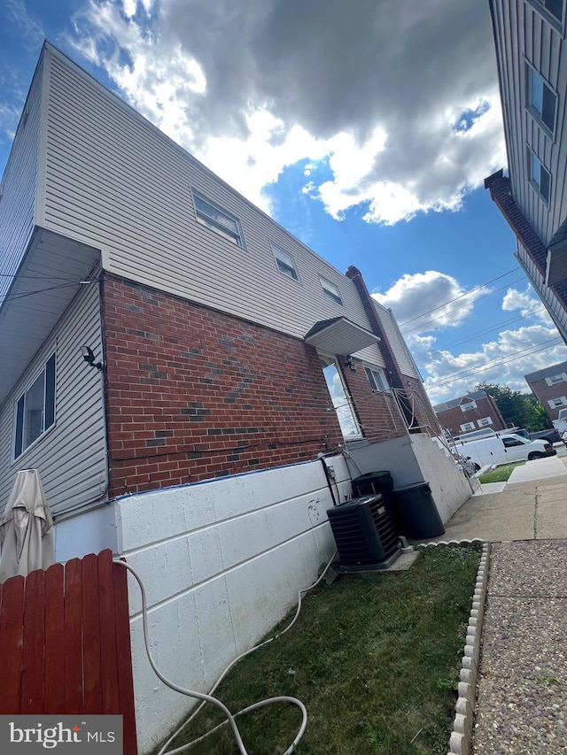 view of property exterior featuring central air condition unit, fence, and brick siding