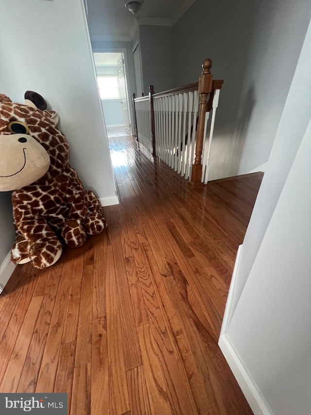 hallway featuring baseboards, ornamental molding, hardwood / wood-style floors, and an upstairs landing