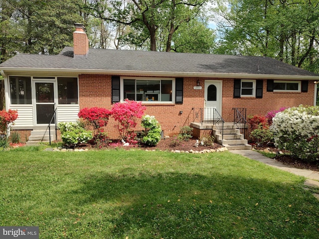 ranch-style house featuring a chimney, a front lawn, a shingled roof, brick siding, and entry steps