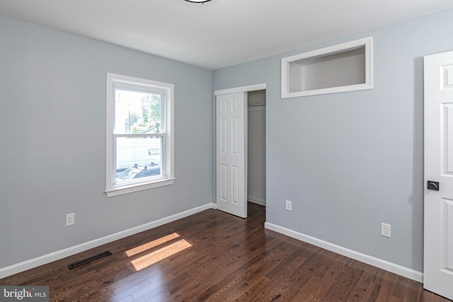 unfurnished bedroom featuring baseboards, a closet, dark wood-style floors, and visible vents