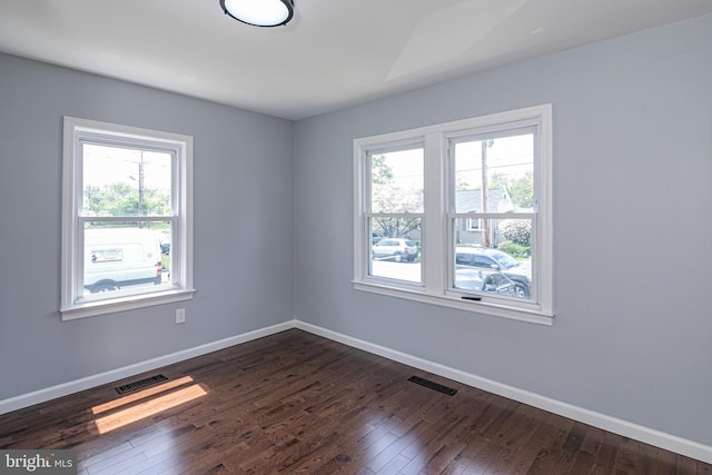 empty room with a wealth of natural light, dark wood finished floors, and visible vents
