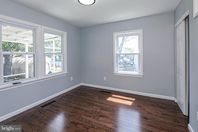 unfurnished bedroom featuring multiple windows, visible vents, and dark wood-type flooring